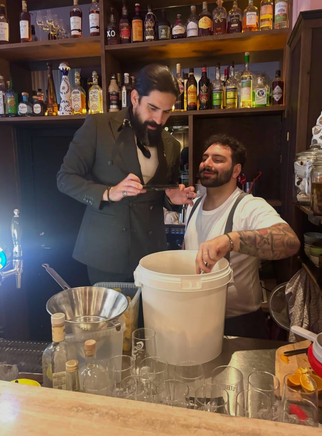 To bartendere i gang bag baren med flaskehylderne bag sig